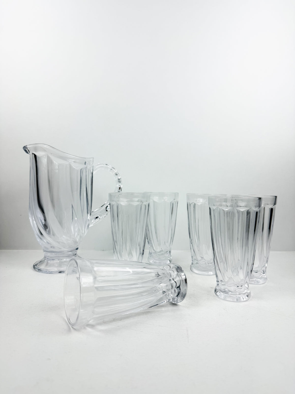 Service en verre transparent composé d'une carafe et de six verres assortis à motifs géométriques.