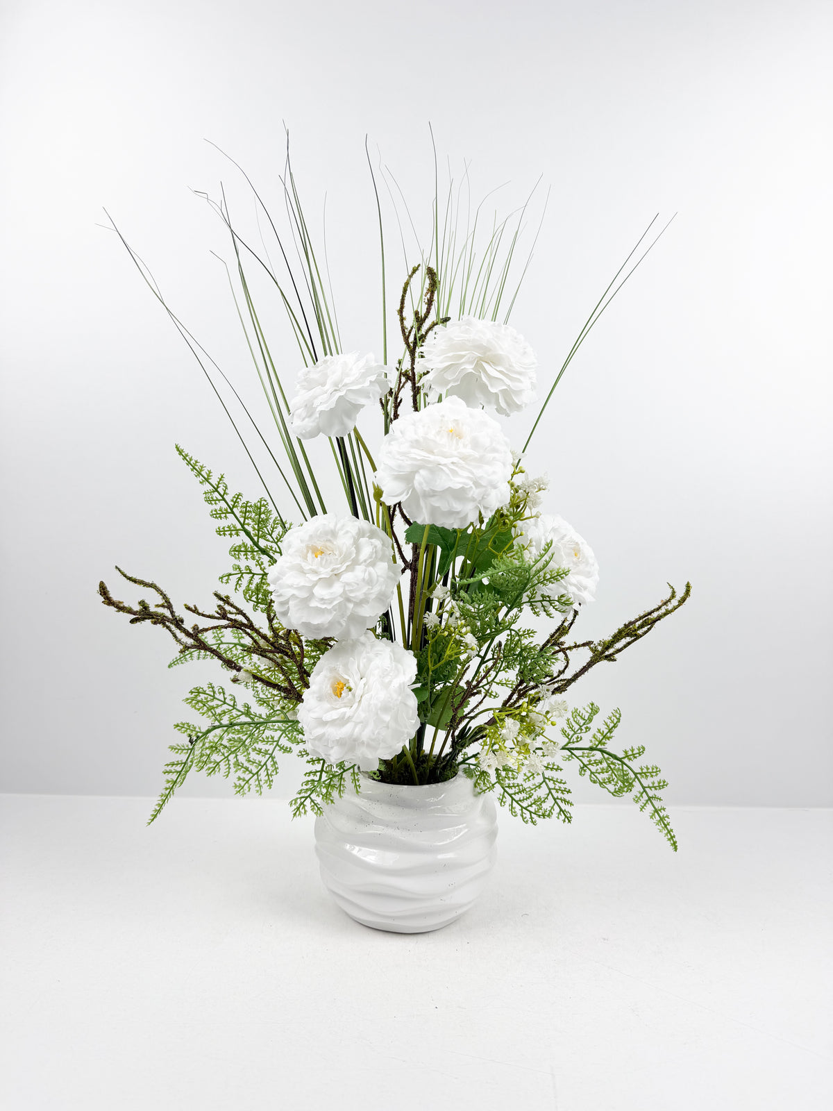 Fleurs blanches raffinées et des touches de verdure délicate dans un magnifique vase en céramique blanche.
