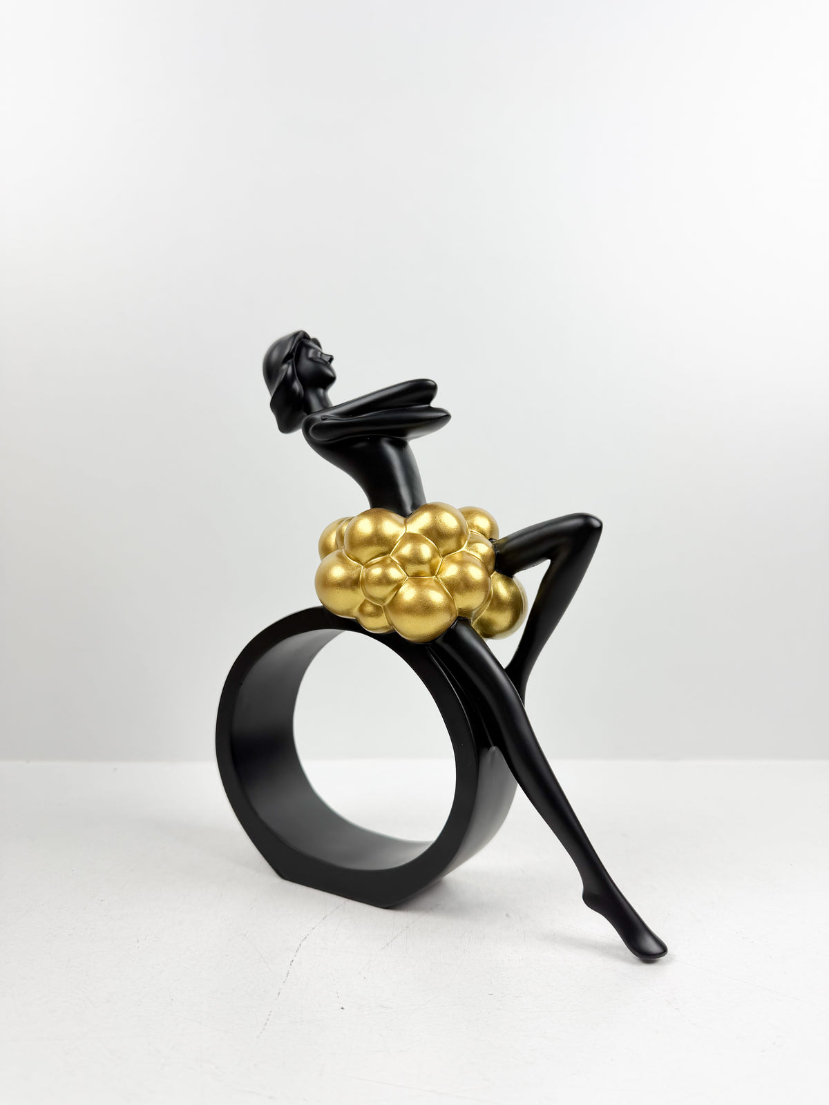 Sculpture décorative en résine noire d'une féminine assise sur un cercle avec détails de sphères dorées.