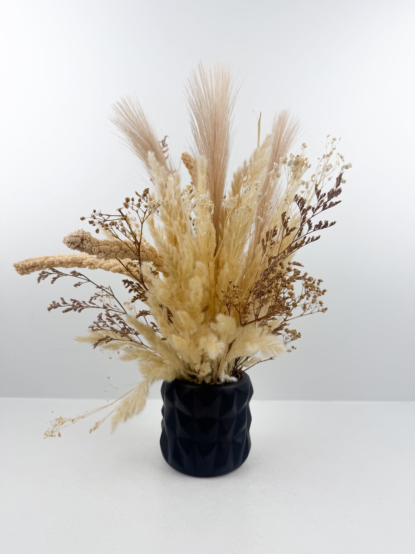Fleurs séchées marron clair arrangées avec élégance dans une vase en céramique noir sophistiquée.