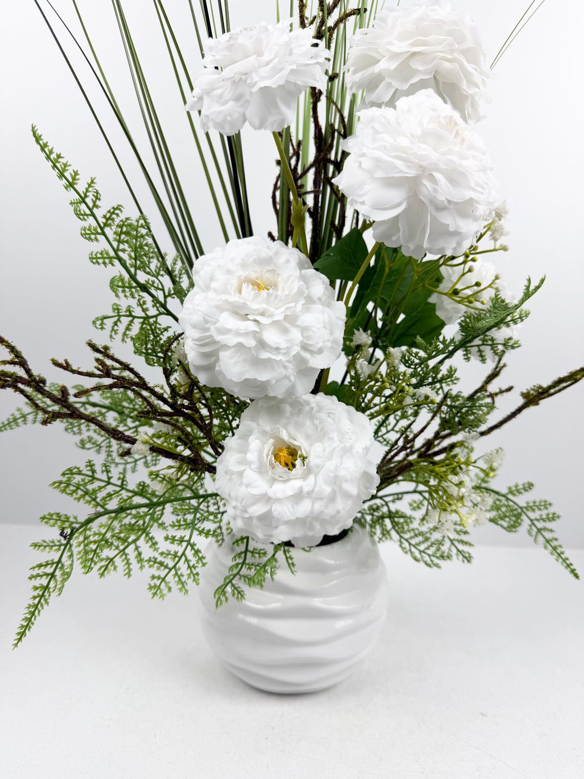 Fleurs blanches raffinées et des touches de verdure délicate dans un magnifique vase en céramique blanche.