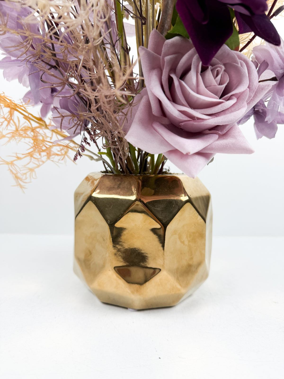 Fleurs séchées délicates dans un élégant vase géométrique en céramique dorée.