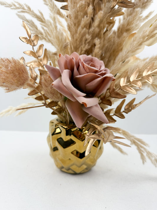 Fleurs séchées rehaussée d'une fleur rose dans un vase en céramique doré aux lignes épurées.